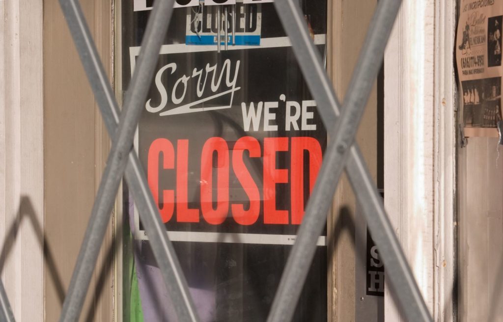 "sorry we're closed" sign on window with gate in front of it