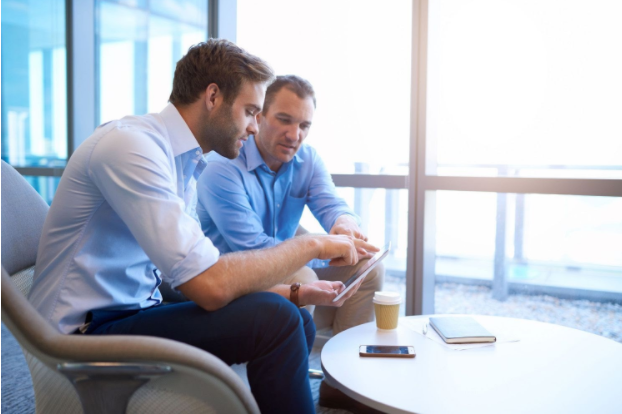 two business man talking looking at ipad in front of windows