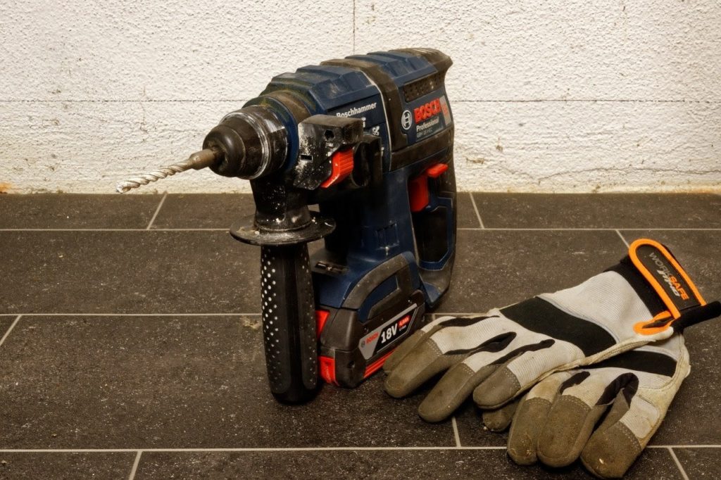screwdriver and pair of work gloves sitting on tile ground in front of white brick wall