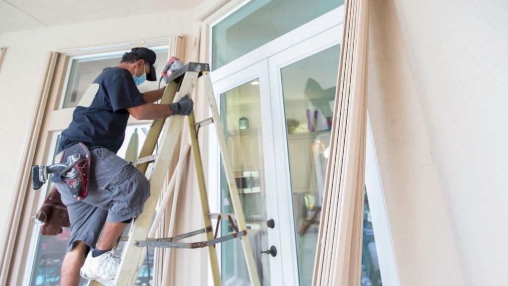 worker on ladder leaned against glass windows of house