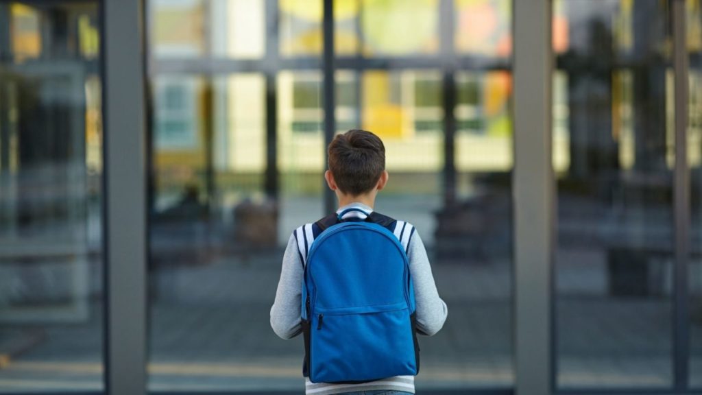 little boy with a blue backpack looking in window building
