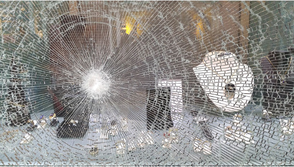 shattered glass window with bullet hole in it looking into a jewelry store